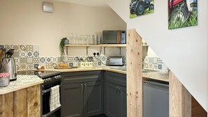 Cocina compacta con gabinetes oscuros, encimera de madera, microondas, tostadora y un lavabo.