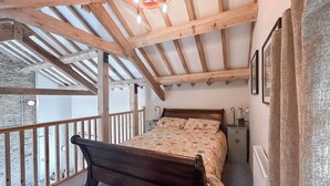 Un dormitorio con techo de madera, una cama, una mesita de noche y ventana con vistas a un balcón.