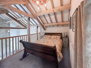 A bedroom with a wooden ceiling, a bed, a nightstand, and a window overlooking a balcony.