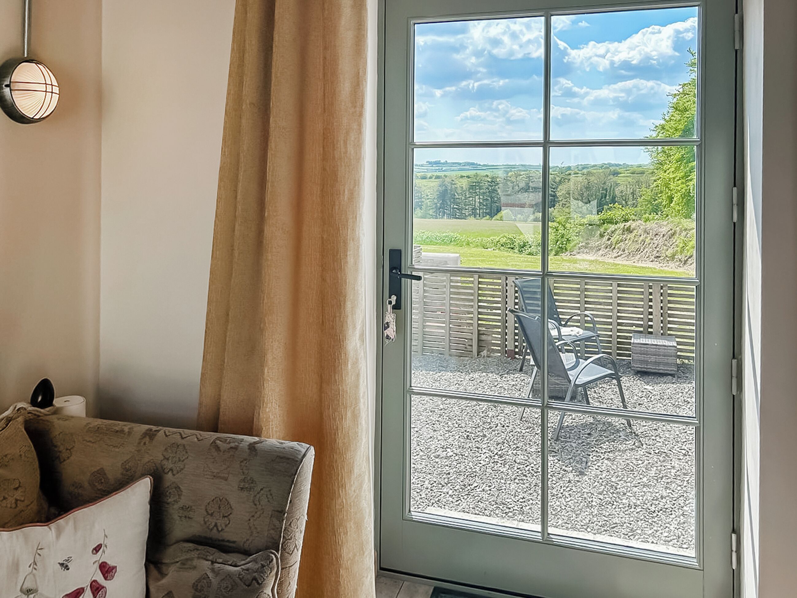 A room with a large window, a sofa, and a view of an outdoor patio area.
