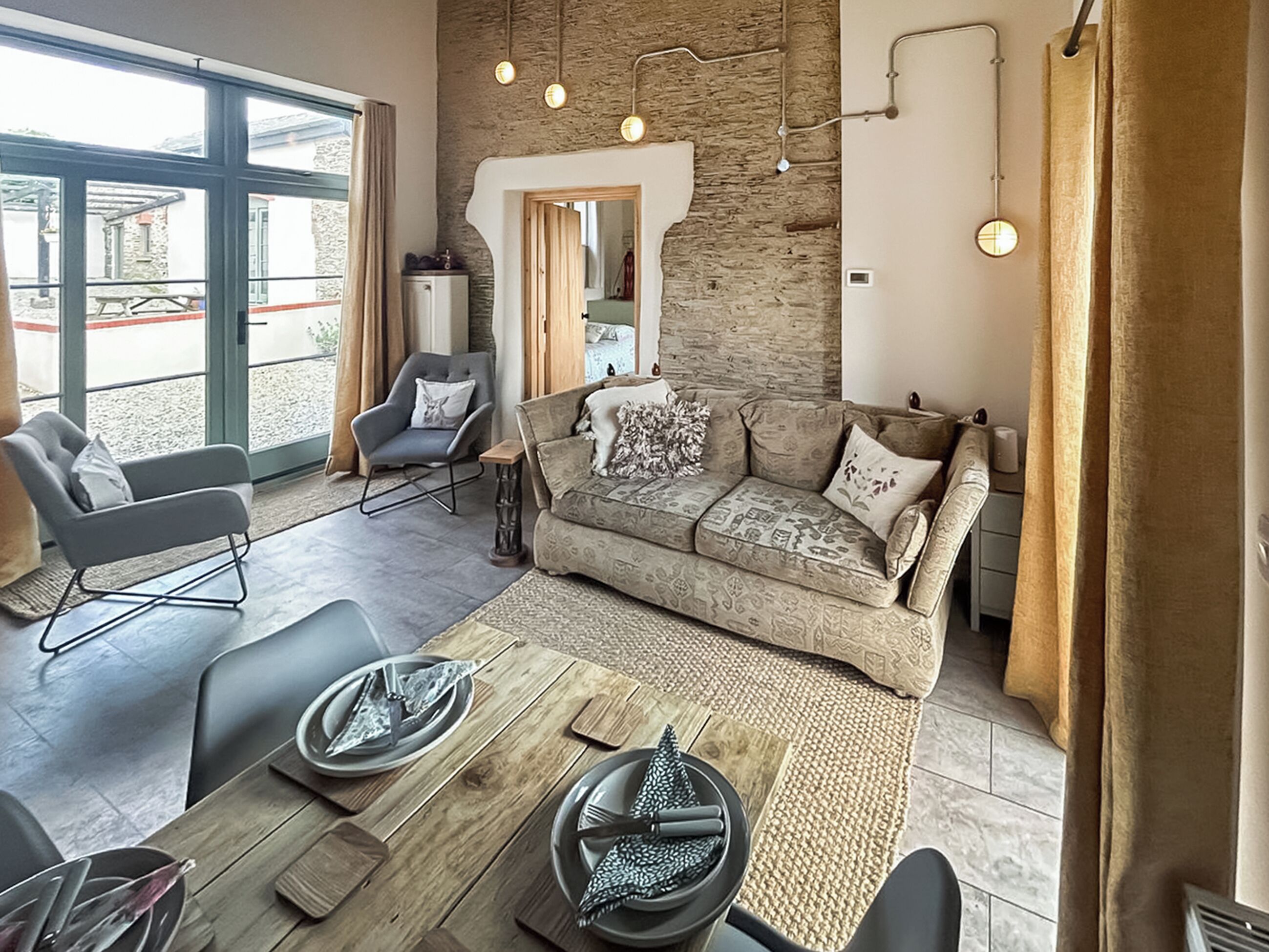 A modern living room with a sofa, chairs, a dining table set for two, and a stone wall.
