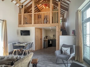 Amplo espaço de estar tipo loft, com pé direito alto, vigas de madeira, área de jantar, cozinha e um espaço de estar aconchegante com lareira.