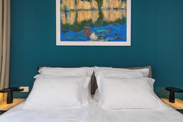 A bed with white linens, two bedside tables, and a painting on the wall.