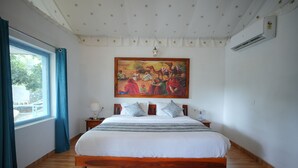 Une chambre avec un grand lit, un tableau accroché au-dessus, une fenêtre avec des rideaux et un appareil de climatisation fixé au mur.