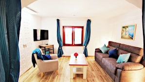 Una sala de estar con sofá, sillón, mesa de centro, televisor y un cuadro en la pared.