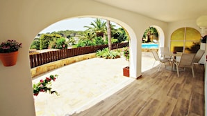 Un patio al aire libre con vista a una piscina y follaje, que incluye una mesa y sillas.
