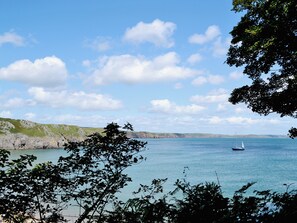 A coastal landscape with a sailboat on the water, rocky cliffs, and greenery.