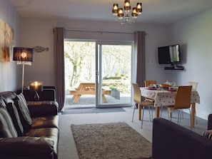 A living room with a sofa, a dining table with chairs, a television, and a sliding glass door leading to an outdoor area.