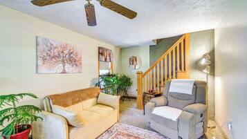 Un salon doté d’un ventilateur de plafond, d’un canapé, d’un fauteuil inclinable, d’une plante en pot et d’un escalier menant à un autre niveau.