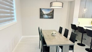 Un comedor con mesa de madera, sillas negras, lámpara colgante y un cuadro en la pared.