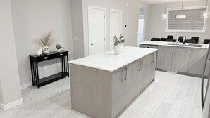Una cocina moderna con una isla central, una mesa consola negra y paredes blancas.