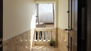 Un pasillo estrecho con suelo de mármol, una puerta de madera a la derecha y un balcón con tejado de metal.