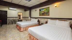 Habitación de hotel con dos camas, piso de baldosas de mármol, techo con azulejos decorativos, un cuadro en la pared y una pequeña mesa con sillas.