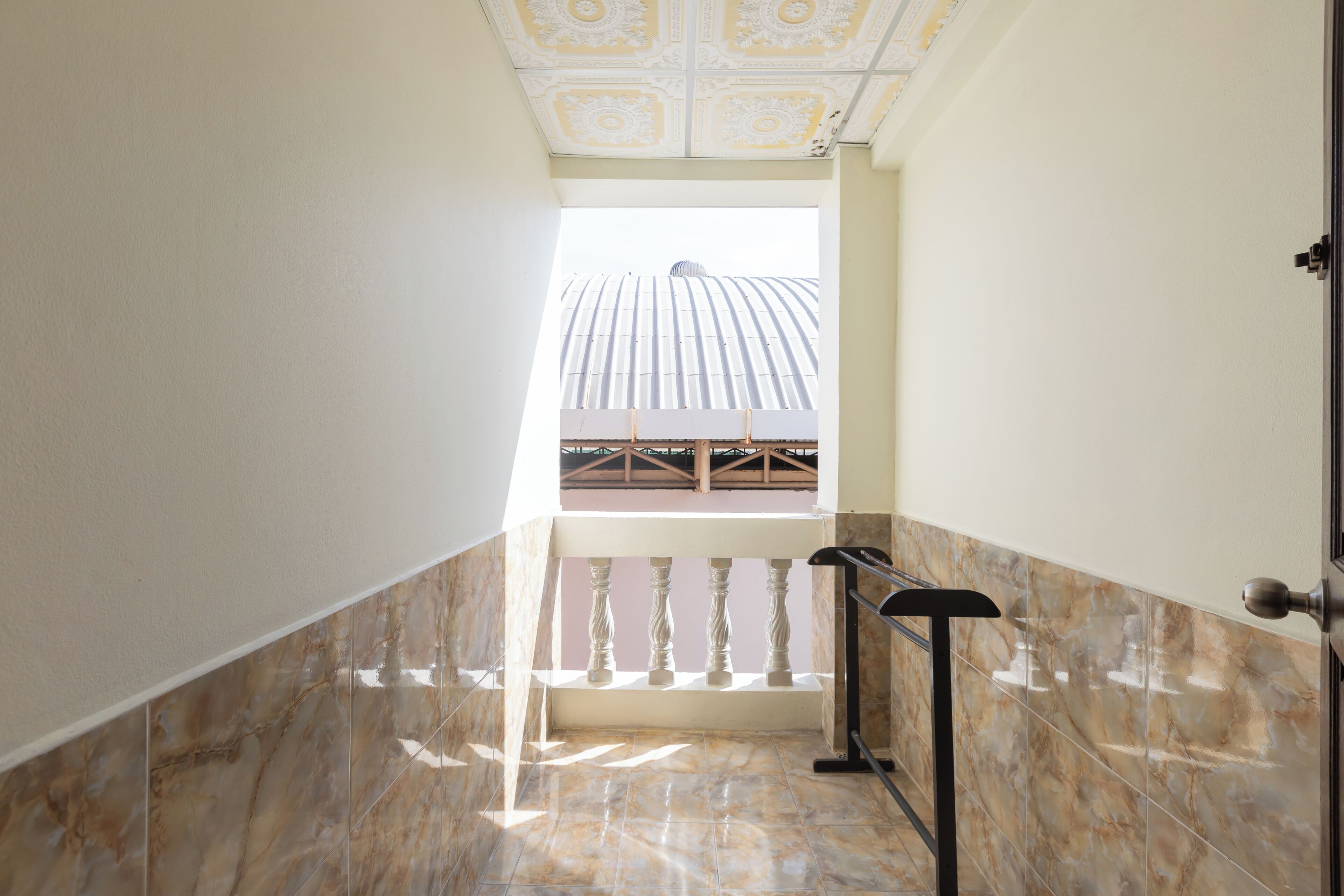 Un couloir au sol en marbre, agrémenté d’une balustrade, d’où l’on peut admirer un bâtiment surmonté d’un dôme.