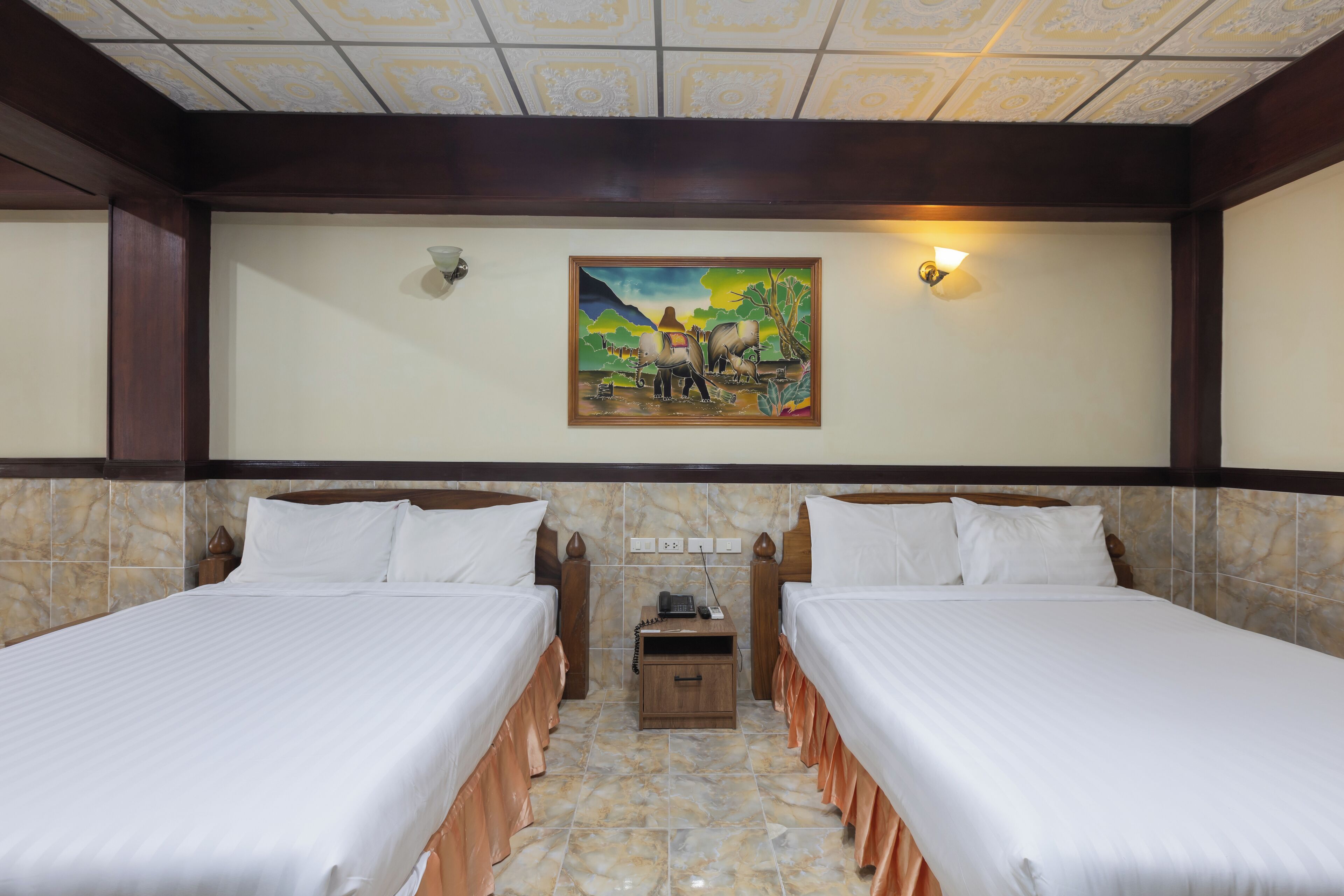 A hotel room with two beds, a nightstand, a painting on the wall, and a ceiling with a patterned design.
