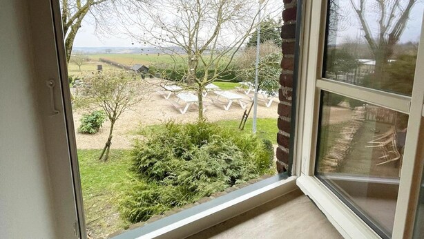 A view from a room with a large window overlooking a garden with picnic tables and a small shed. - Holiday Home in Voerendaal With Terrace (Voerendaal)