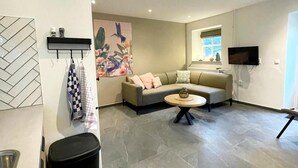 A modern living room with a grey sofa, a round coffee table, and a large abstract painting on the wall. - Holiday Home in Voerendaal With Terrace (Voerendaal)