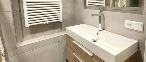 A modern bathroom with a white sink, wooden vanity, and a mirror above the sink.