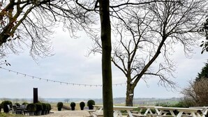 An outdoor seating area with picnic tables and string lights, surrounded by trees and a gravel path. - Holiday Home in Voerendaal With Terrace (Voerendaal)
