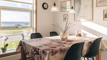 A dining area with a table set for two, a vase with branches, and framed artwork on the wall.