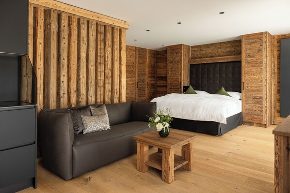 A modern bedroom with a wooden accent wall, a dark sofa, a wooden coffee table, and a bed with white bedding and green pillows. - Vacation apartment 2, 55sqm, for comfort without thresholds (Reit im Winkl)