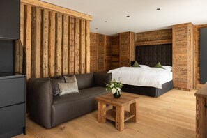 A modern bedroom with a wooden accent wall, a dark sofa, a bed with white bedding, and a small wooden table with a vase of flowers. - Vacation apartment 2, 55sqm, for comfort without thresholds (Reit im Winkl)