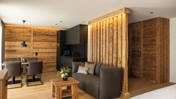 A modern room with a wooden floor, a sofa, a dining table with chairs, and a kitchen area. - Vacation apartment 2, 55sqm, for comfort without thresholds (Reit im Winkl)