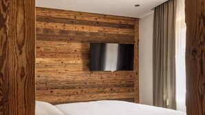 A bedroom with a wooden headboard, a flat-screen TV mounted on the wall, a bed with white bedding, and a wooden floor. - Vacation apartment 9, 50sqm, your place to feel good (Reit im Winkl)