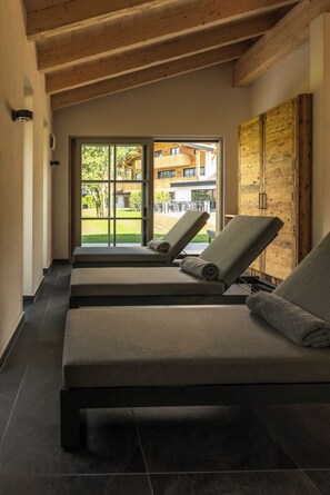 A spa room with two reclining chairs, a wooden ceiling, and a view of a building and greenery outside.