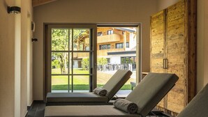 Una stanza spa con due poltrone reclinabili, soffitto in legno e vista su un edificio e vegetazione.