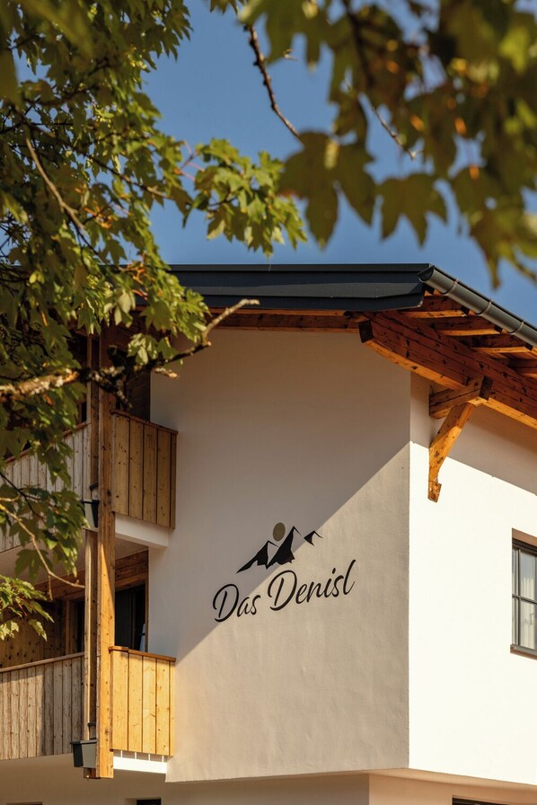 A building with a sign reading "Das Denisl" and a balcony with wooden railings.