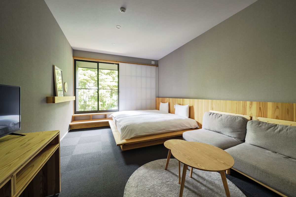 A modern hotel room with a bed, sofa, TV, and a large window.