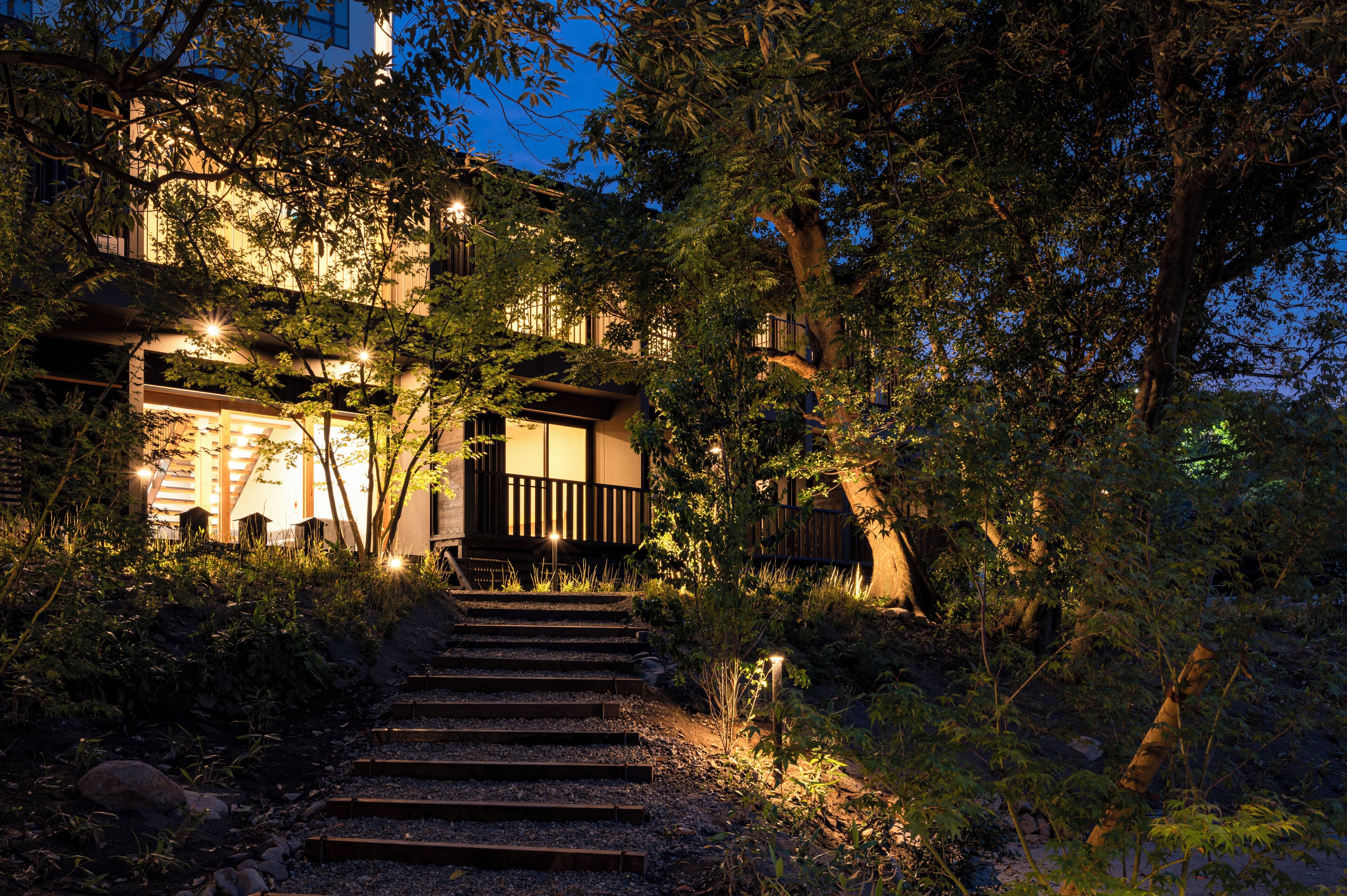 Un bâtiment doté d’un escalier menant à une terrasse en bois, entouré d’arbres et de végétation.