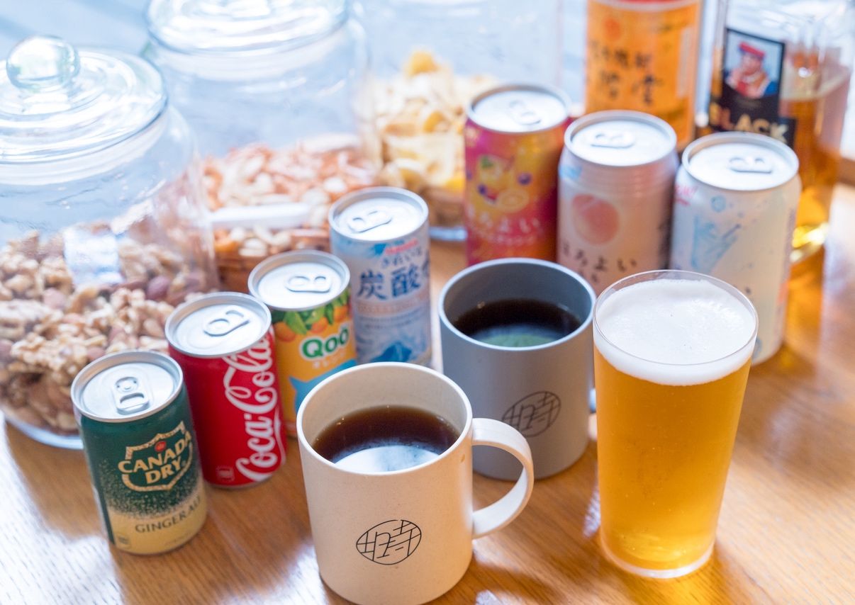 A variety of beverages including cans, mugs, and a glass of beer on a table.