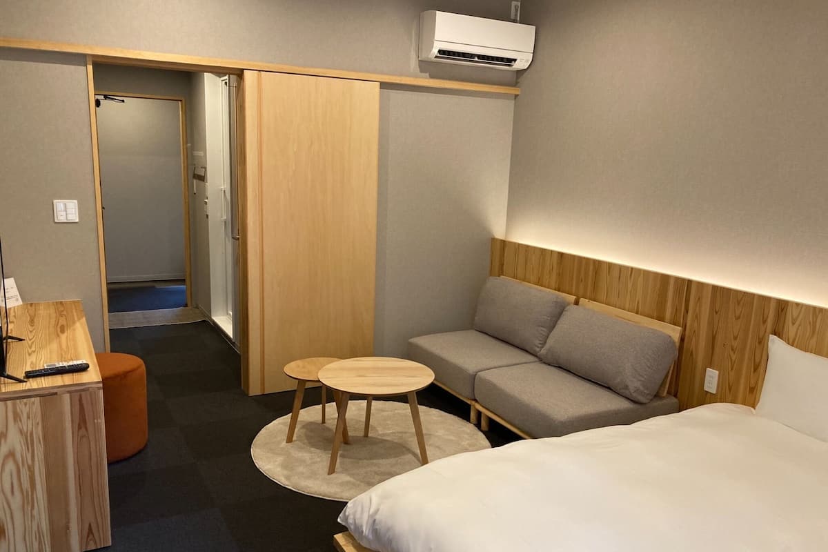 A hotel room with a bed, a sofa, a small table, and a desk with a remote control.
