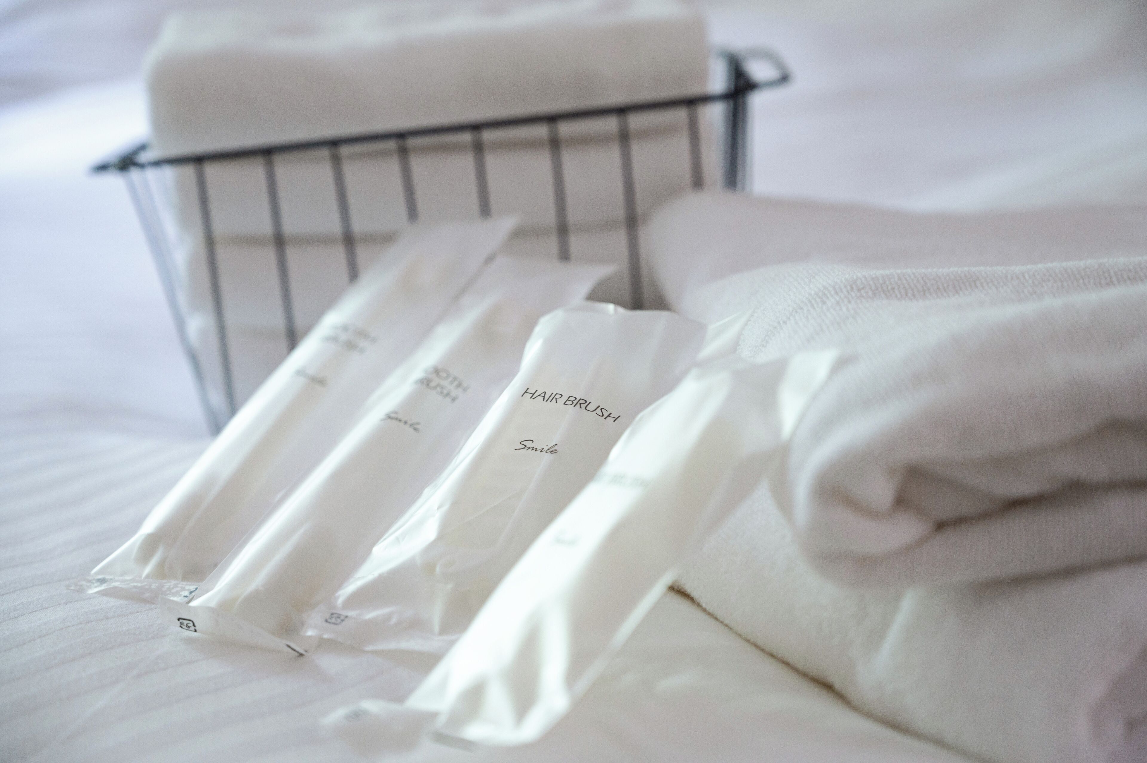 A metal basket containing neatly folded white towels and a hair brush.