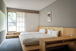 A modern hotel room with two beds, a wooden desk, a large window, and a framed picture on the wall.