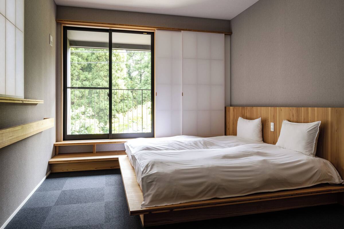 A bedroom with a wooden bed, a large window with a view of trees, and a sliding door.