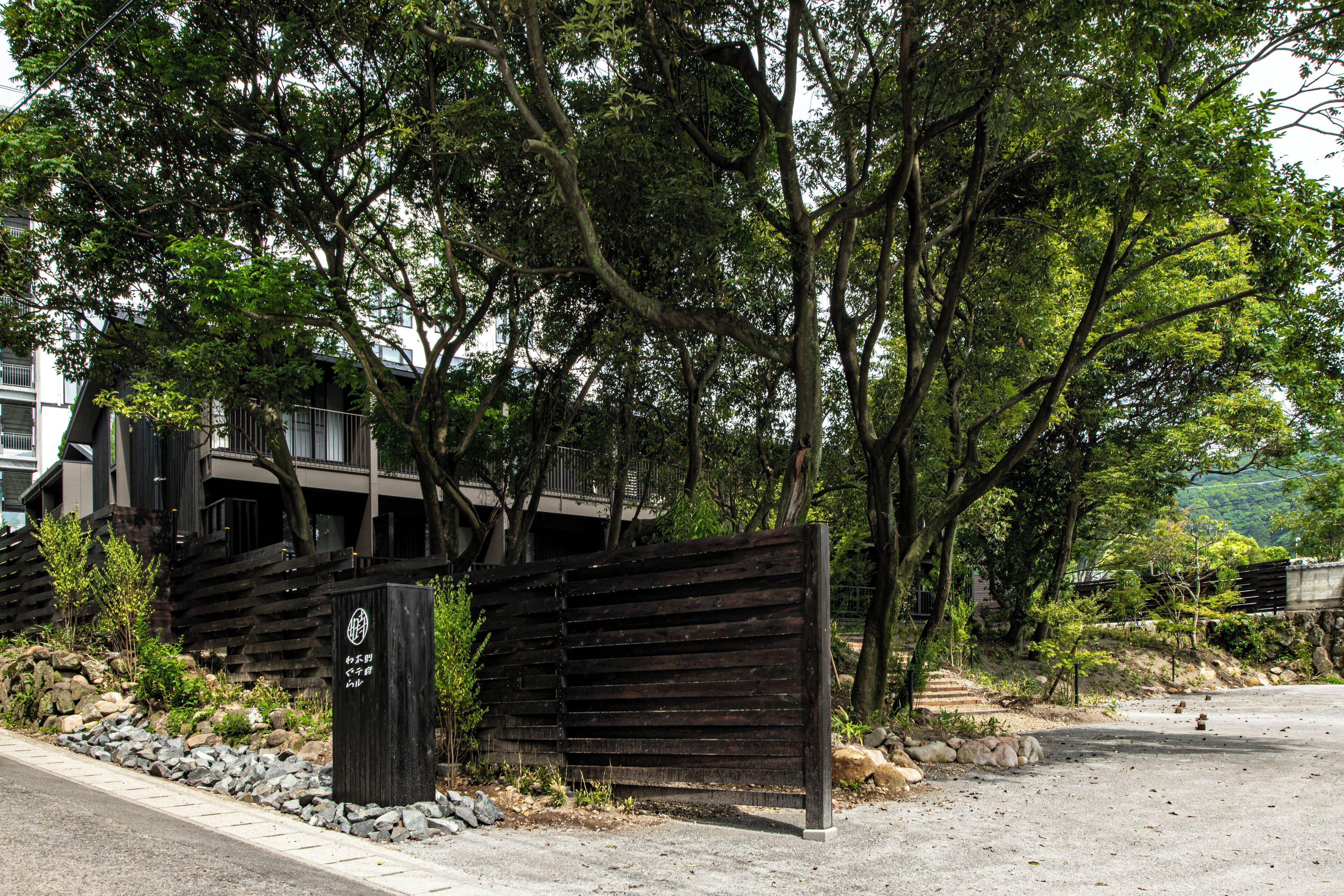 A gated entrance with a wooden fence, a paved pathway, and a building with multiple floors in the background.