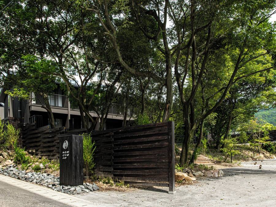 A gated entrance with a wooden fence, a paved pathway, and a building with multiple floors in the background.