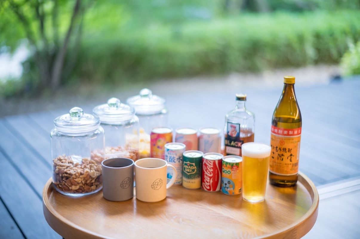 A wooden tray with various food and drink items, including jars, cans, and bottles, on an outdoor surface.