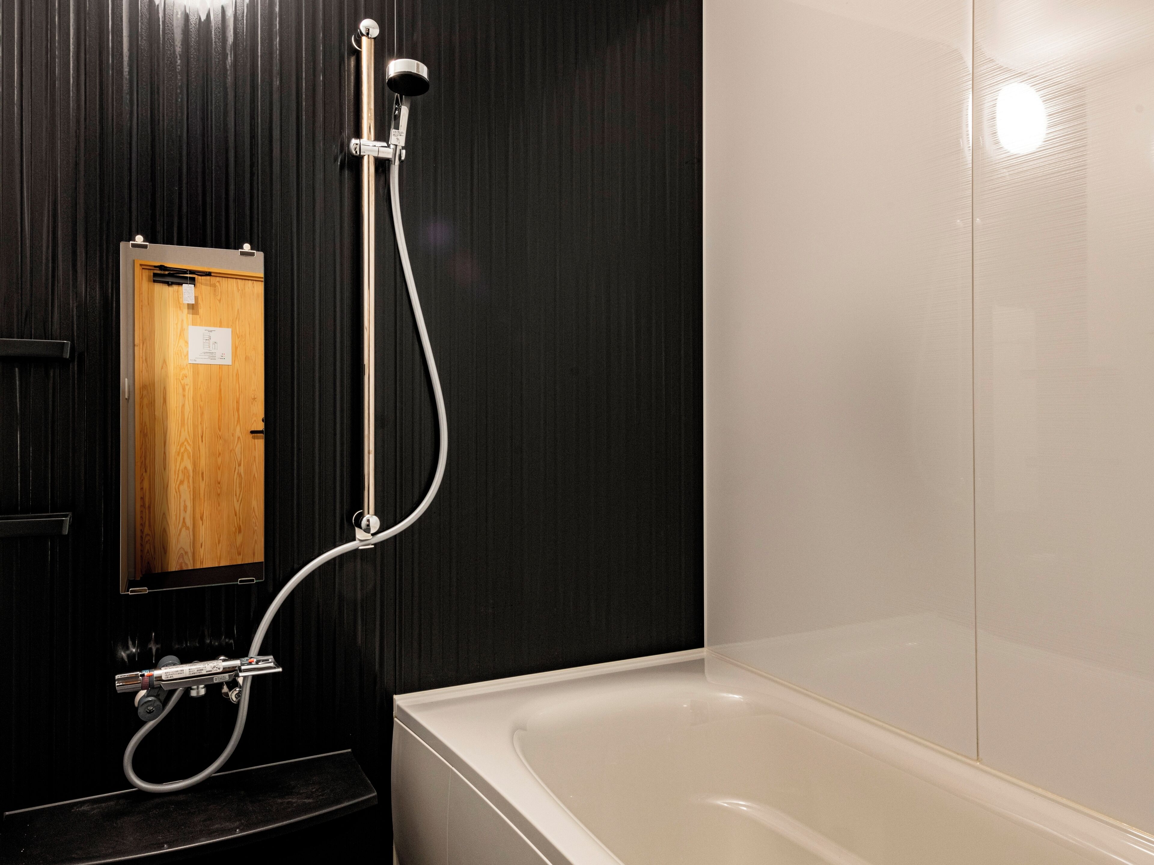 A modern bathroom with a bathtub, a shower with a handheld showerhead, and a wooden door.