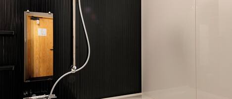 A modern bathroom with a bathtub, a shower with a handheld showerhead, and a wooden door.