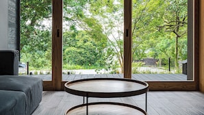 A room with a large window, a round wooden table, and a grey sofa. - Beppu Hotel Negura (Beppu)