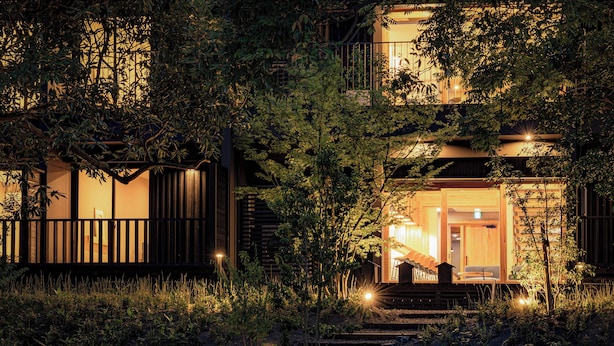 A two-story wooden house with a balcony, surrounded by dense foliage. - Beppu Hotel Negura (Beppu)