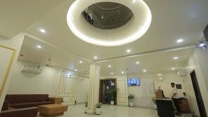 A modern lobby with a circular skylight, a reception desk, seating area, and potted plants. - Jeel Pearl Hotel (Udaipur)