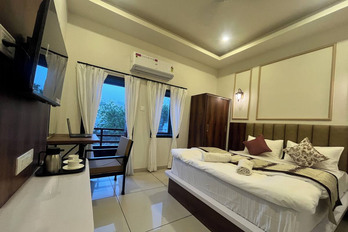 A hotel room with a bed, a desk with a laptop, a TV, and an air conditioning unit.