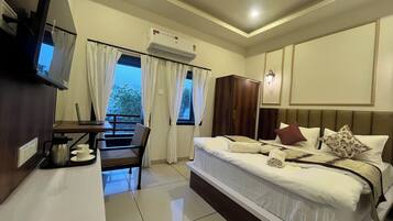 A hotel room with a bed, a desk with a laptop, a TV, and an air conditioning unit.