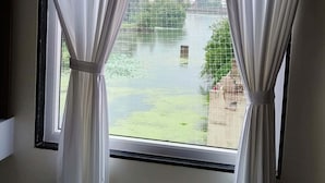 A window with white curtains, a view of a water body, and buildings in the background. - Jeel Pearl Hotel (Udaipur)