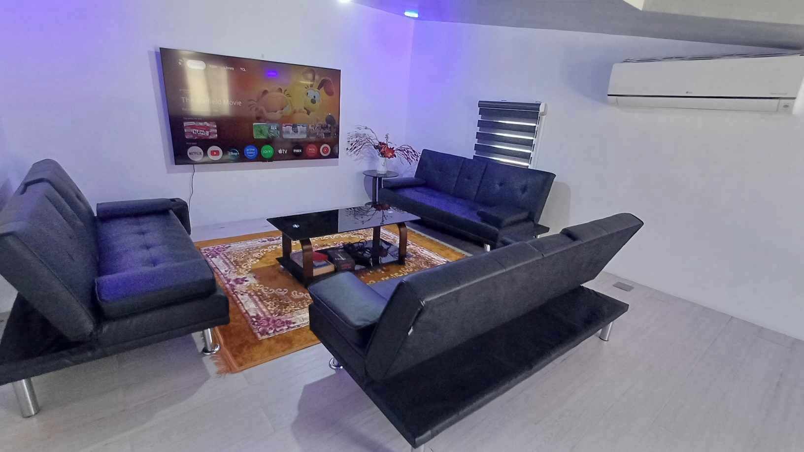 Una sala moderna con televisor de pantalla plana, un sofá, una mesa de centro y una planta decorativa.